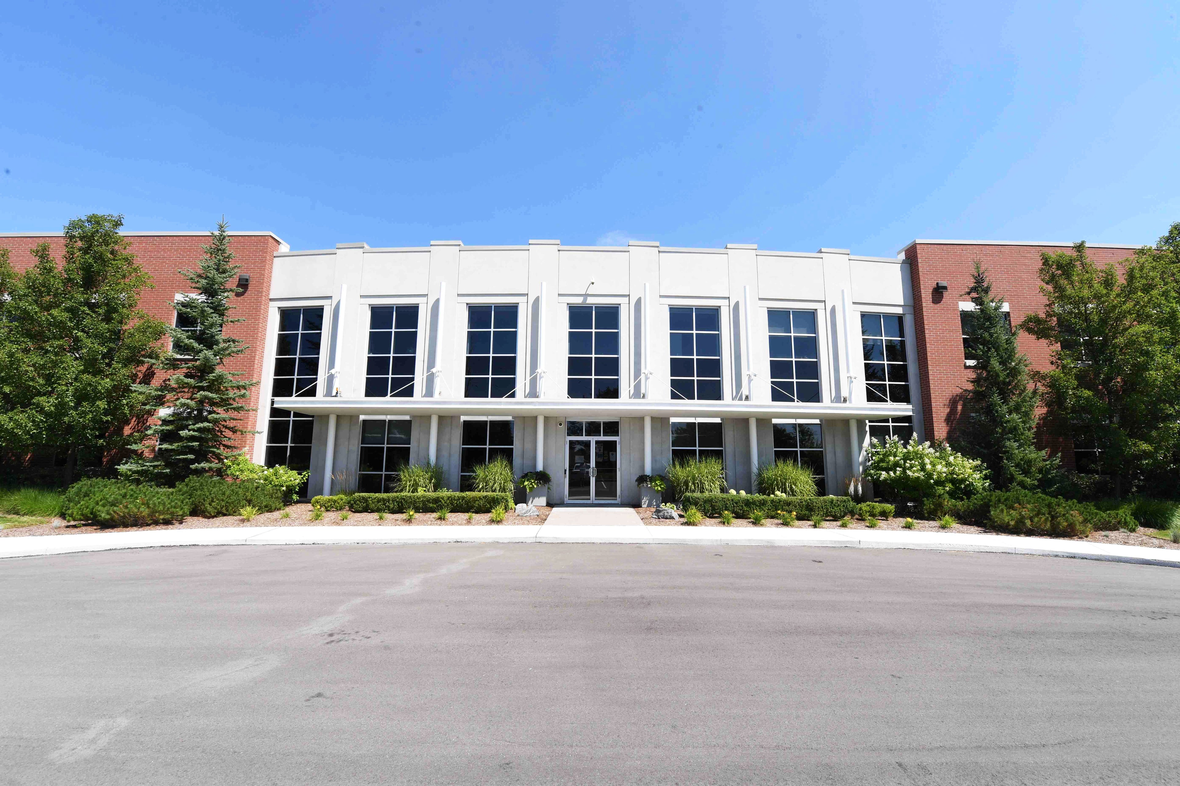 Modern office building with white facade and large windows, surrounded by trees on a clear day.